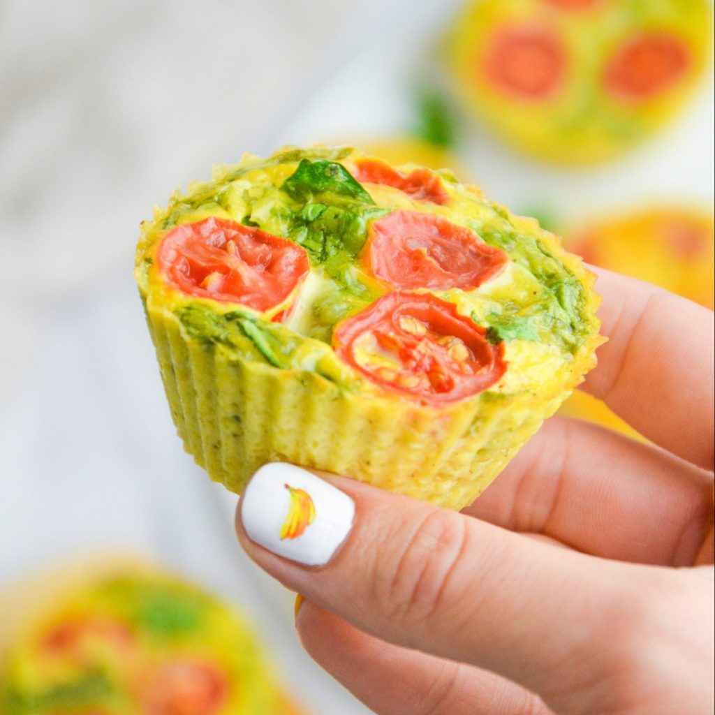 hand holding an egg savory egg muffin with spinach and tomato