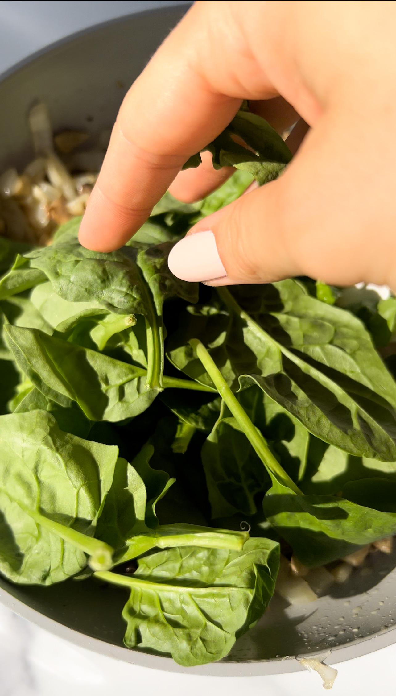 adding fresh spinach to a pan