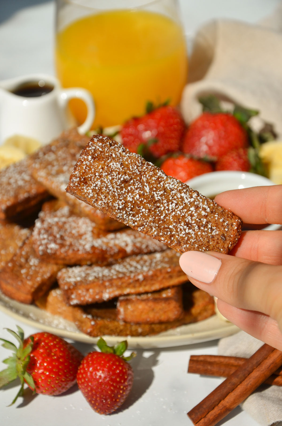 A hand holding up a vegan french toast stick up over the plate.