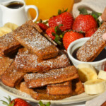 A plate of french toast sticks on the table with one dipping in maple syrup.
