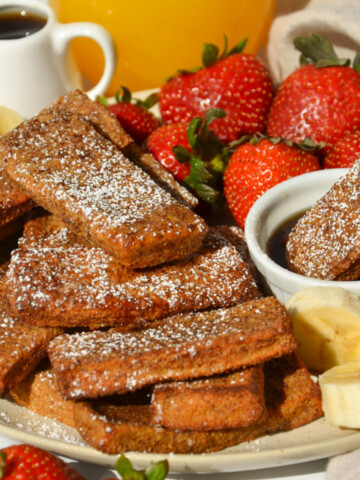 A plate of french toast sticks on the table with one dipping in maple syrup.