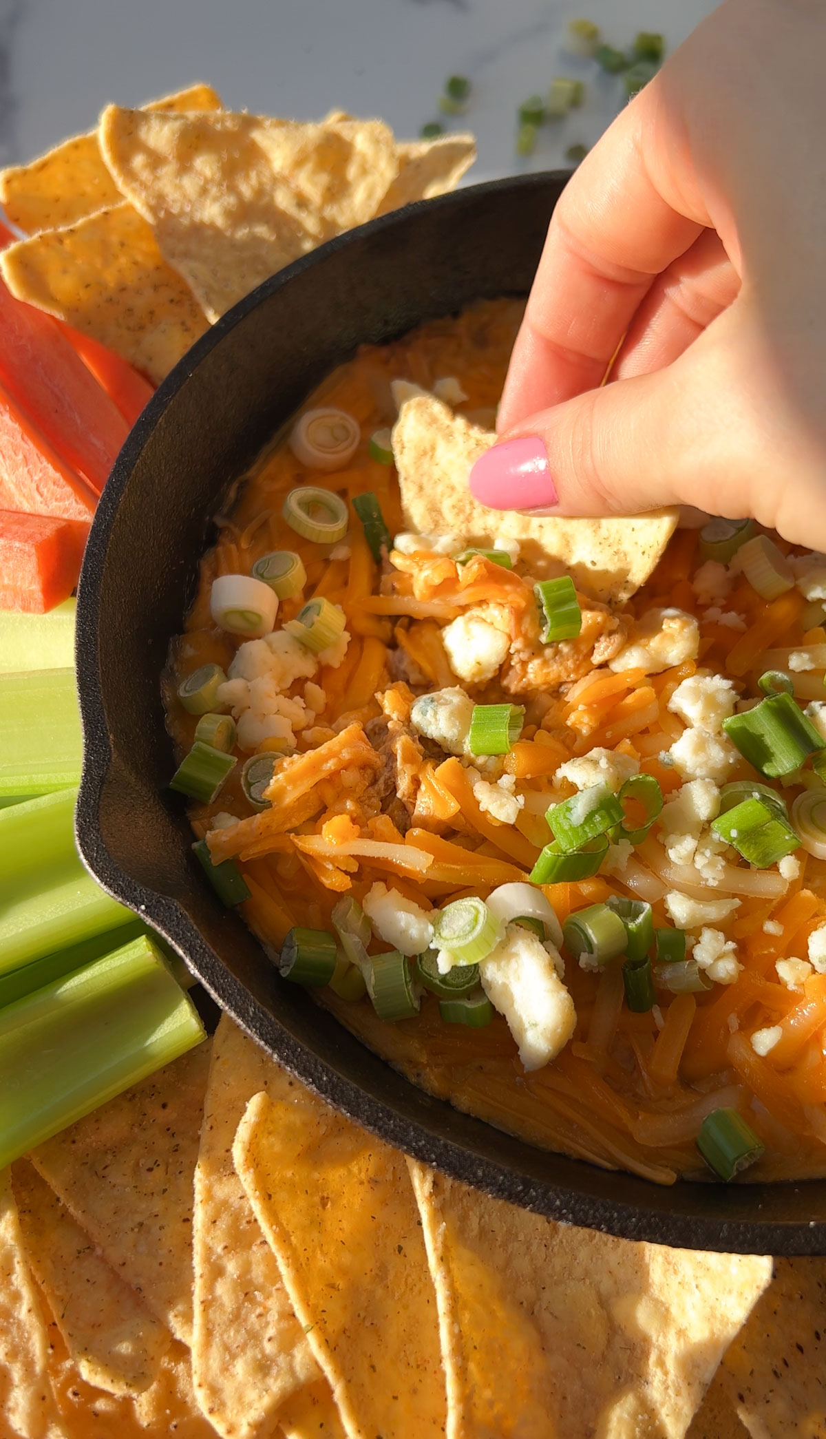 A skillet of vegan buffalo chicken dip on the table with chips and veggie sticks.