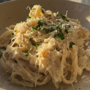 Fettuccine alfredo noodles in a bowl topped with a bit of parsley.