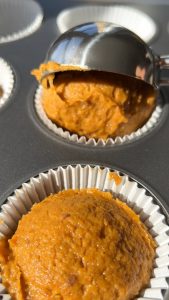 adding a scoop of pumpkin cupcake batter to a muffin tin