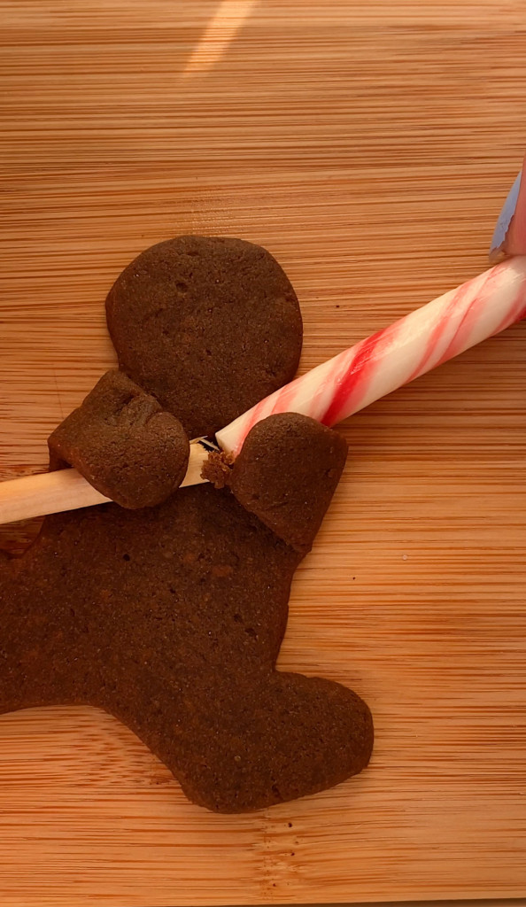 placing a candy cane in the hands of a vegan gingerbread cookie