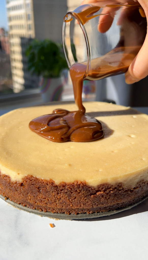 pouring salted caramel on top of a salted caramel cheesecake