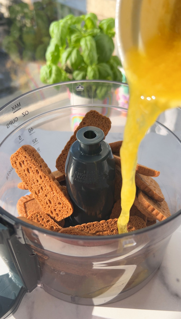 adding vegan butter to a food processor with biscoff cookies