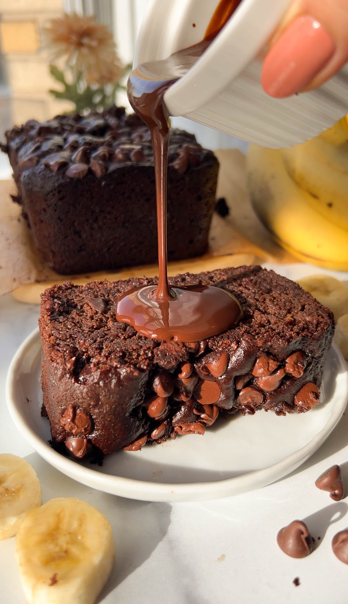 pouring chocolate over a slice of double chocolate banana bread