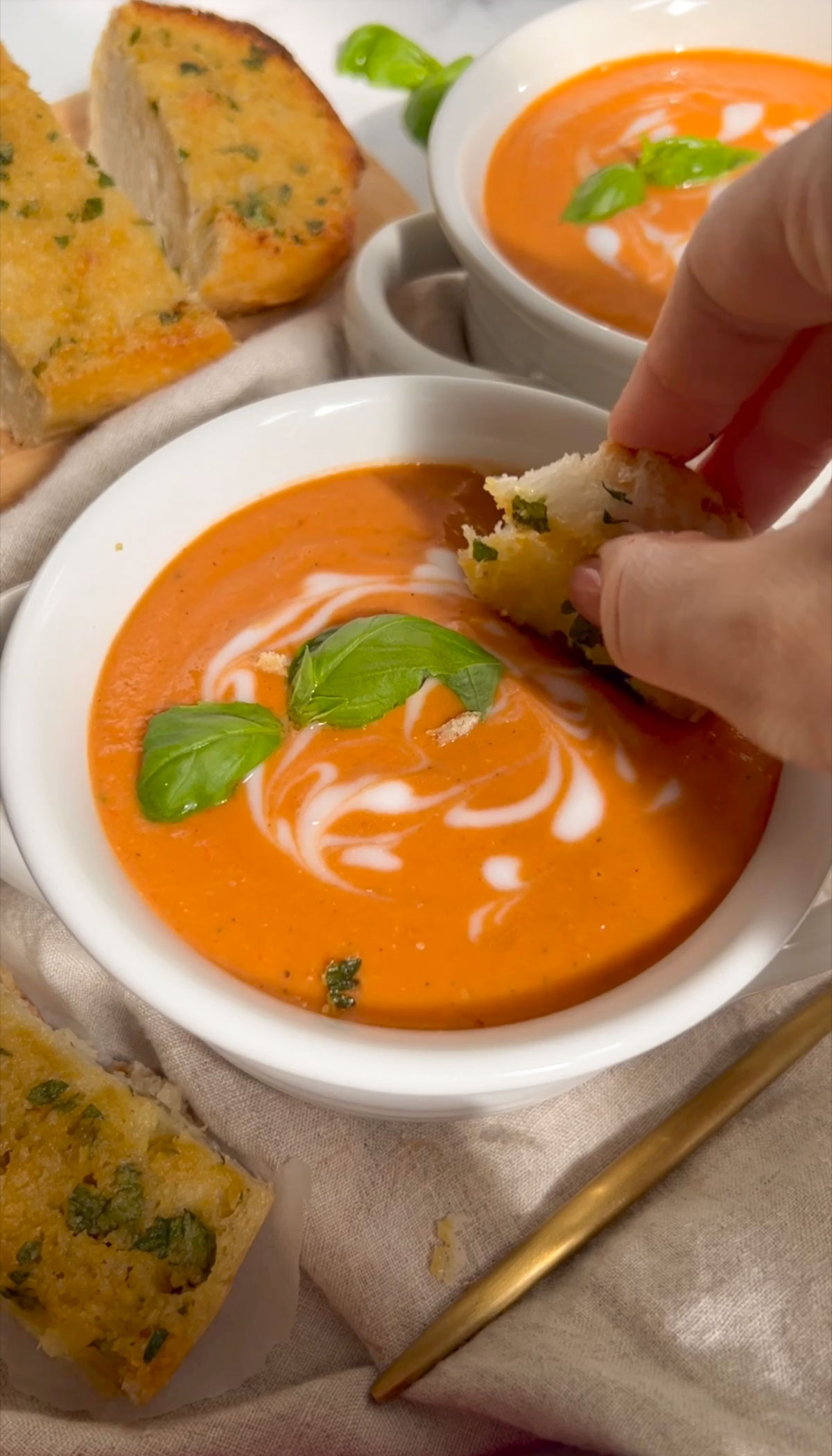 roasted red pepper and tomato soup in a bowl with a hand dipping garlic bread in it