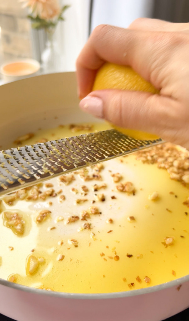 zesting a lemon in a pan with olive oil and roasted garlic