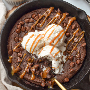 overhead shot of vegan black bean brownie in a skillet with ice cream and caramel sauce on top