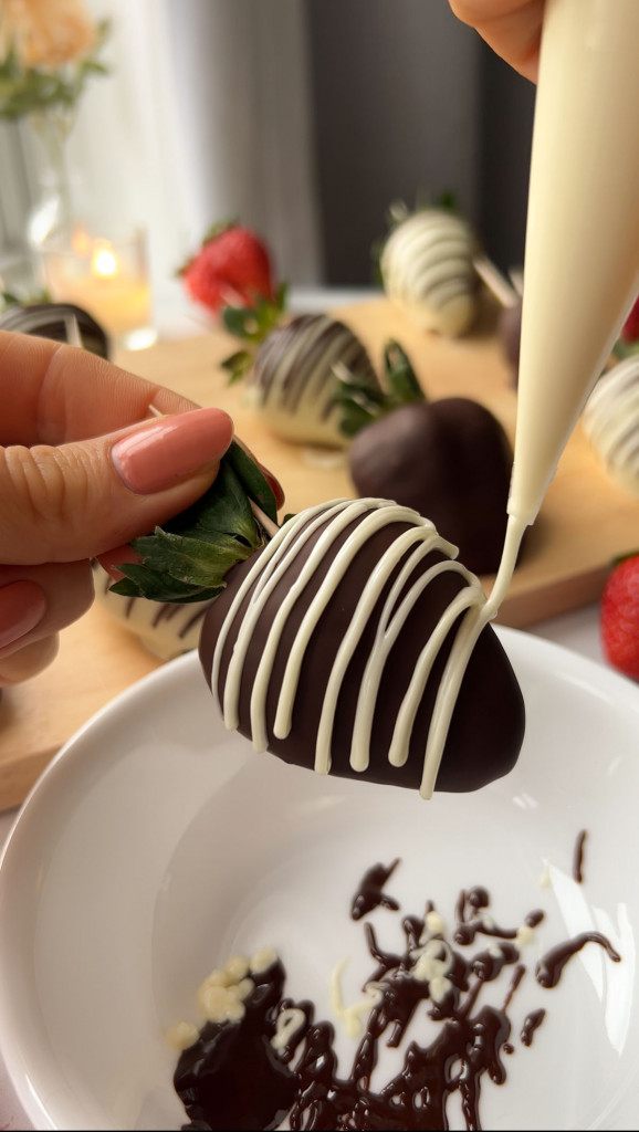 drizzling white chocolate over a dark chocolate covered strawberry