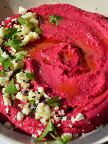 roasted beet hummus on a plate topped with vegan feta, fresh parsley, and sesame seeds