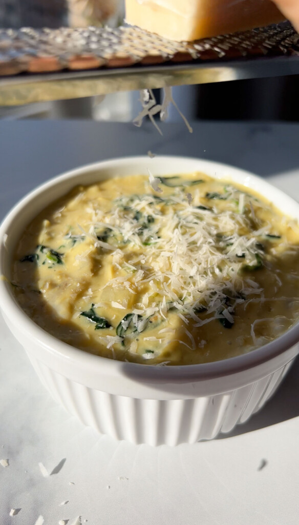 grating vegan parmesan cheese in a bowl of spinach dip