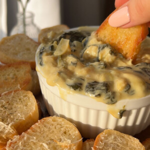 dipping a piece of bread in a bowl of spinach dip