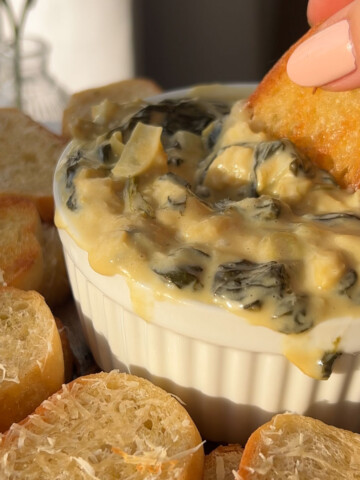 dipping a piece of bread in a bowl of spinach dip