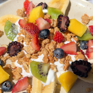 banana split on a plate with yogurt, granola, and fruit on top