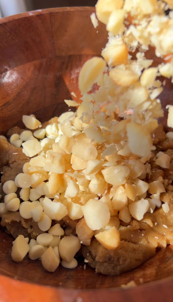 adding chopped macadamia nuts to a large wooden bowl