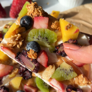 A hand holding a piece of yogurt bark with fruit on top.