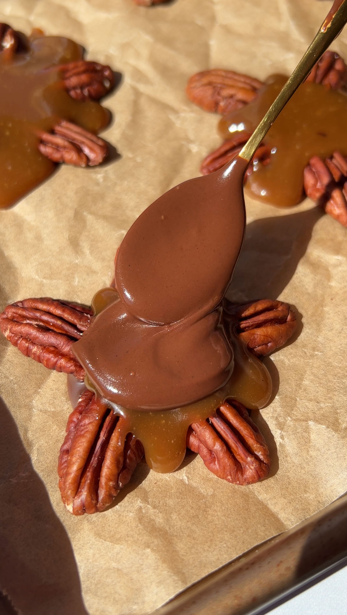 Spooning chocolate on top of the caramel and pecans.