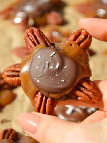 A hand holding a vegan chocolate turtle up over the tray.