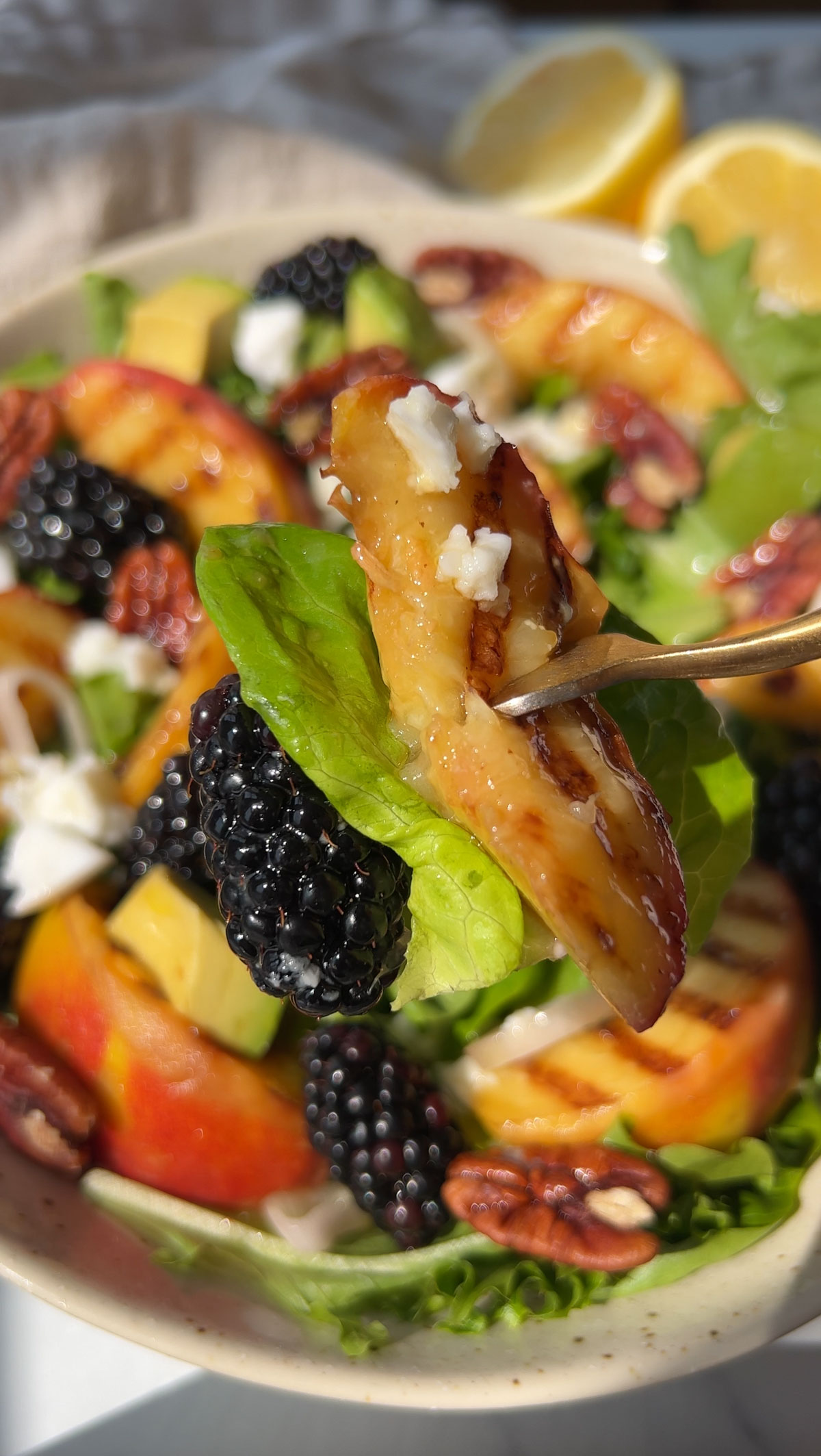 A fork holding a grilled peach up over the bowl of salad.