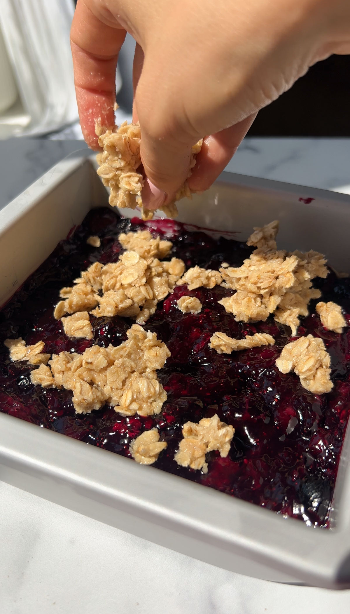 Adding the oatmeal mixture to the top of the blueberry crumble bars.