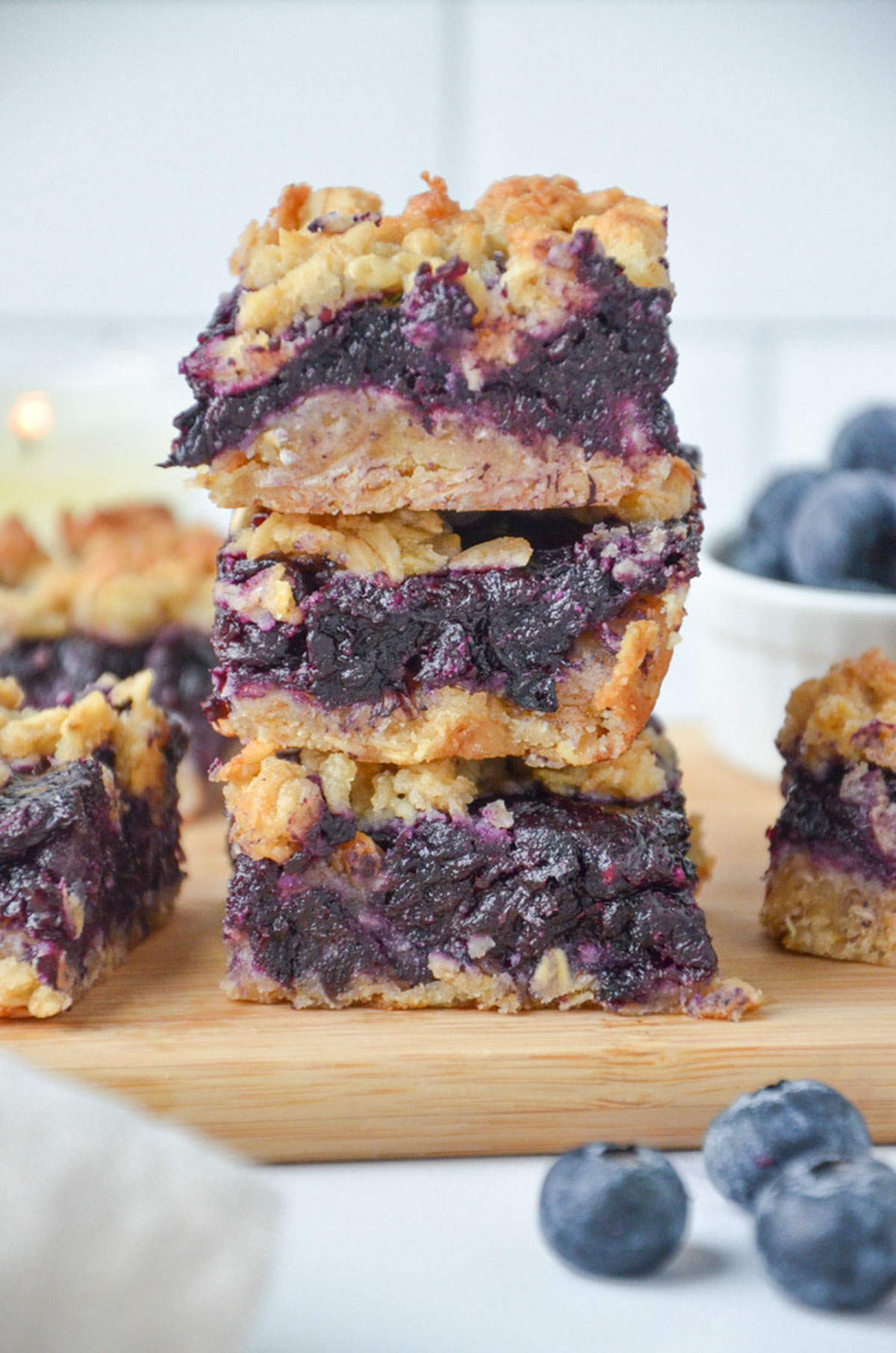 A stack of Starbucks copycat blueberry oatmeal bars on a wooden platter with fresh blueberries scattered around. 