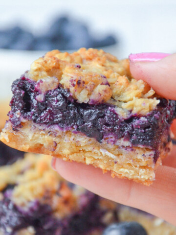 A hand holding a Starbucks blueberry oatmeal bar up over the plate.