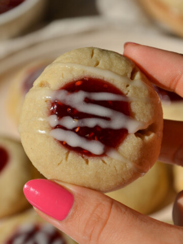 Vegan and gluten-free thumbprint cookie held up by two fingers over the plate.