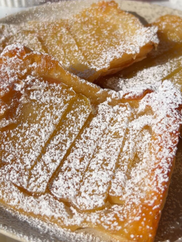 Two apple puff pastry danish on a plate sprinkled with powdered sugar.
