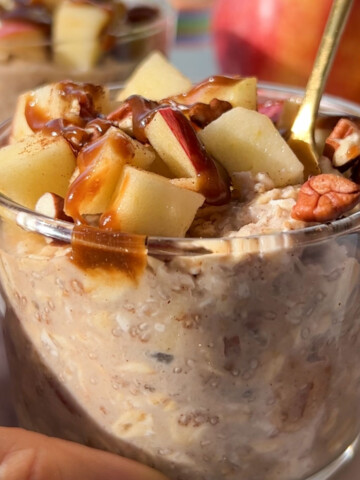 Gluten free overnight oats in a glass with apples on top and a hand wrapped around it.