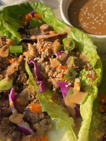 Vegan lettuce wraps on the table next to a small bowl of peanut sauce.