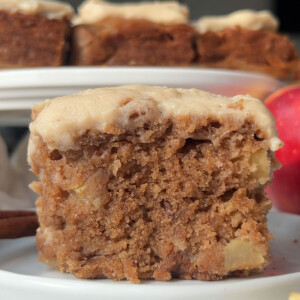 A piece of vegan apple cake on a plate with more pieces in the background.