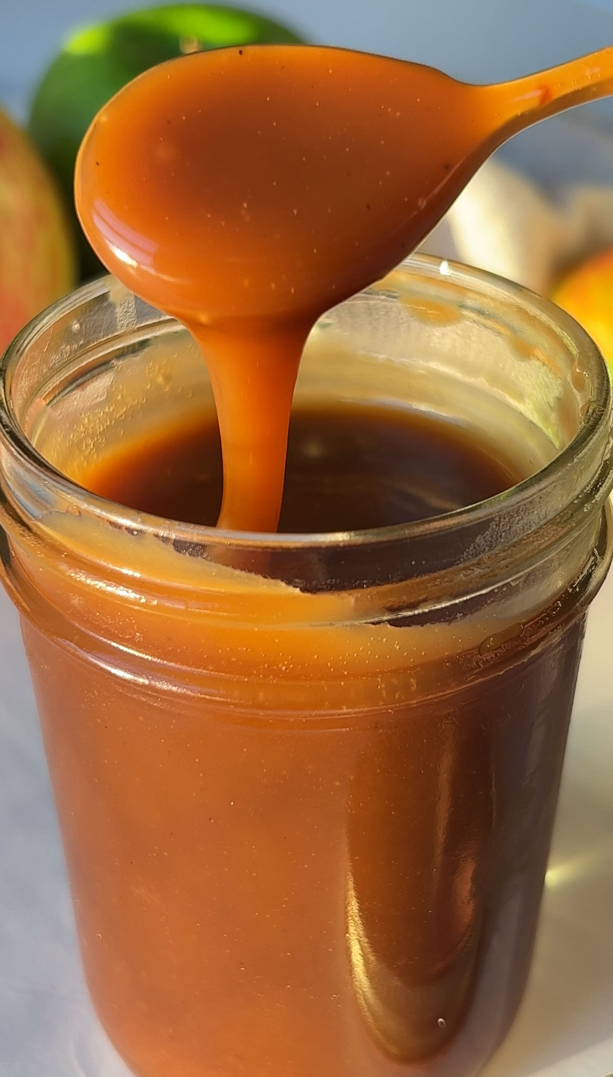 A jar of vegan caramel sauce with a spoon lifting up a bit to drizzle back into the jar.