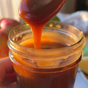 A jar of vegan caramel sauce with a spoon drizzling back into the jar.