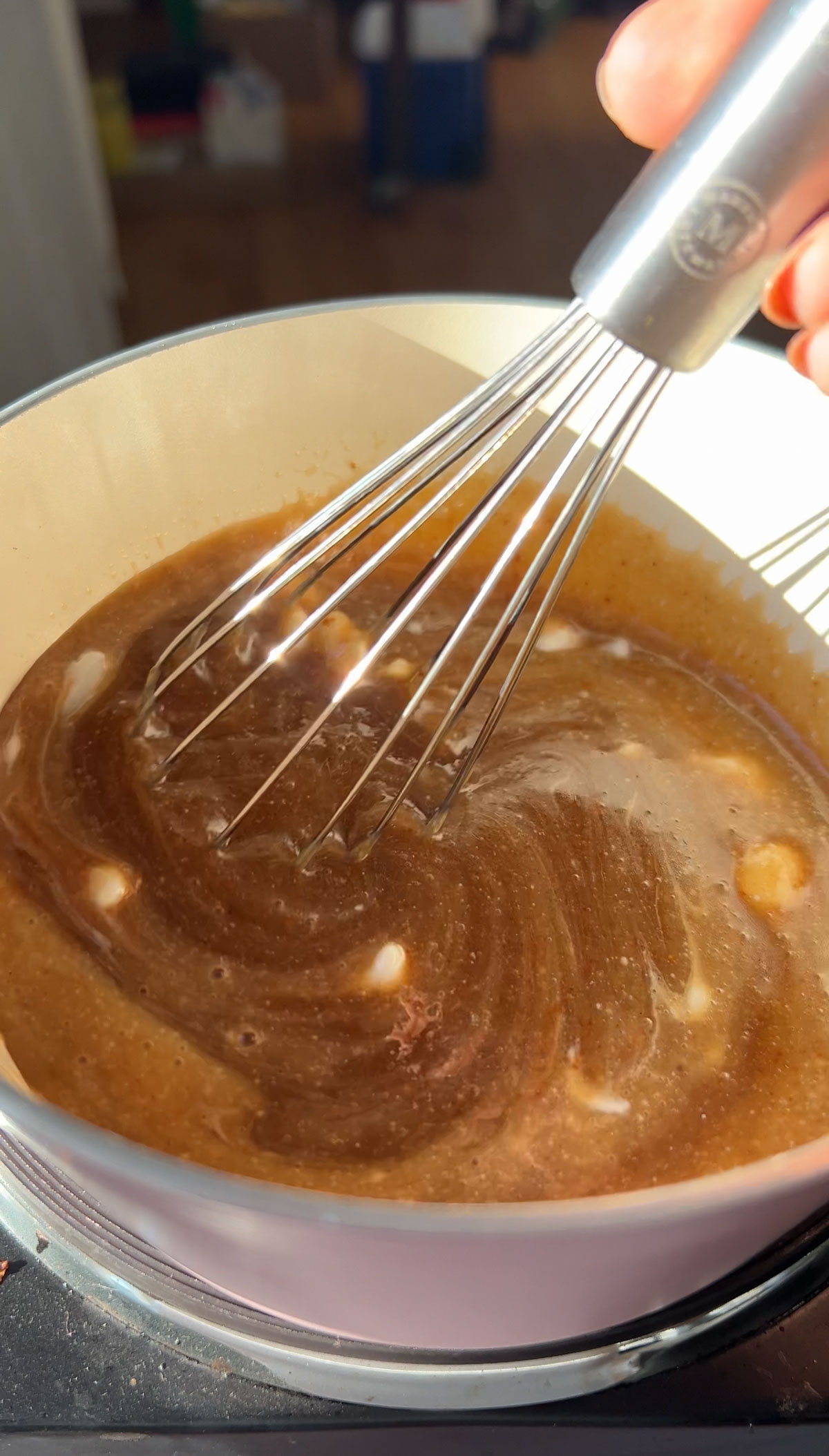 A whisk stirring vegan caramel sauce in a pot.