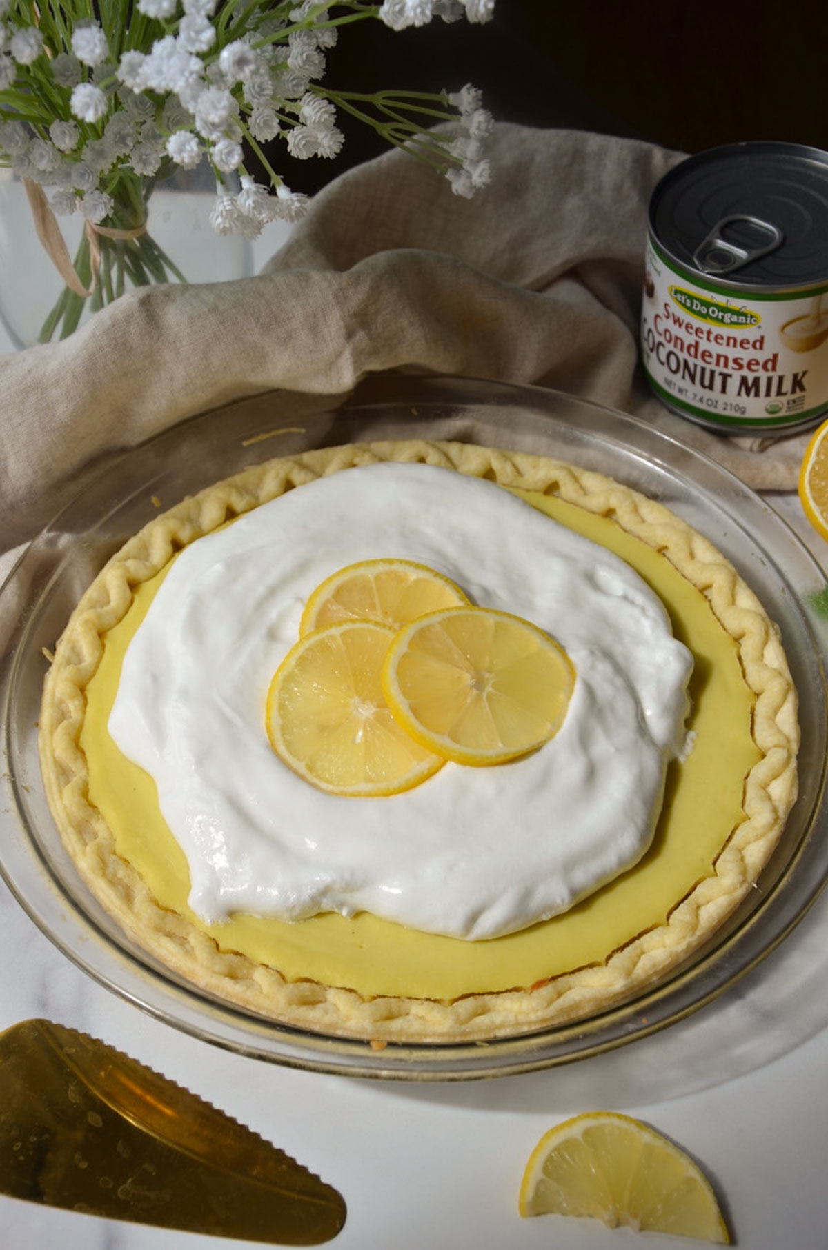 A whole vegan lemon pie on the table topped with whipped cream and lemon slices.