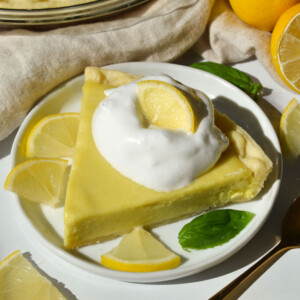 An high angle shot of a piece of lemon pie on a plate with a piece of mint and whipped cream.