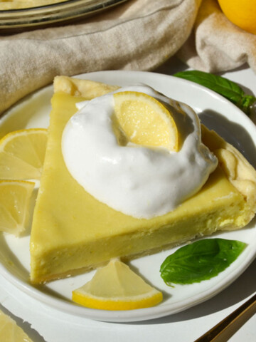 An high angle shot of a piece of lemon pie on a plate with a piece of mint and whipped cream.