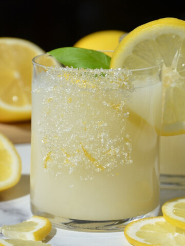 Creamy lemonade in a glass with sugar and zest on the side and garnished with a lemon slice.