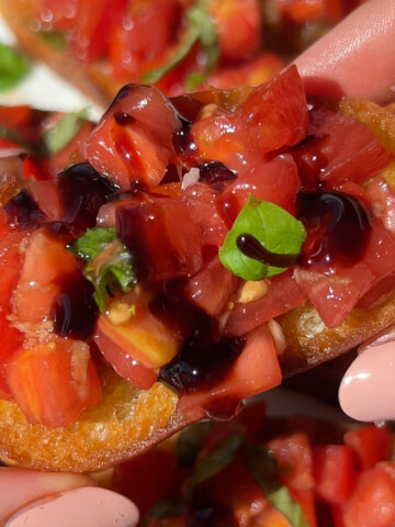 A piece of vegan bruschetta held up with two hands.