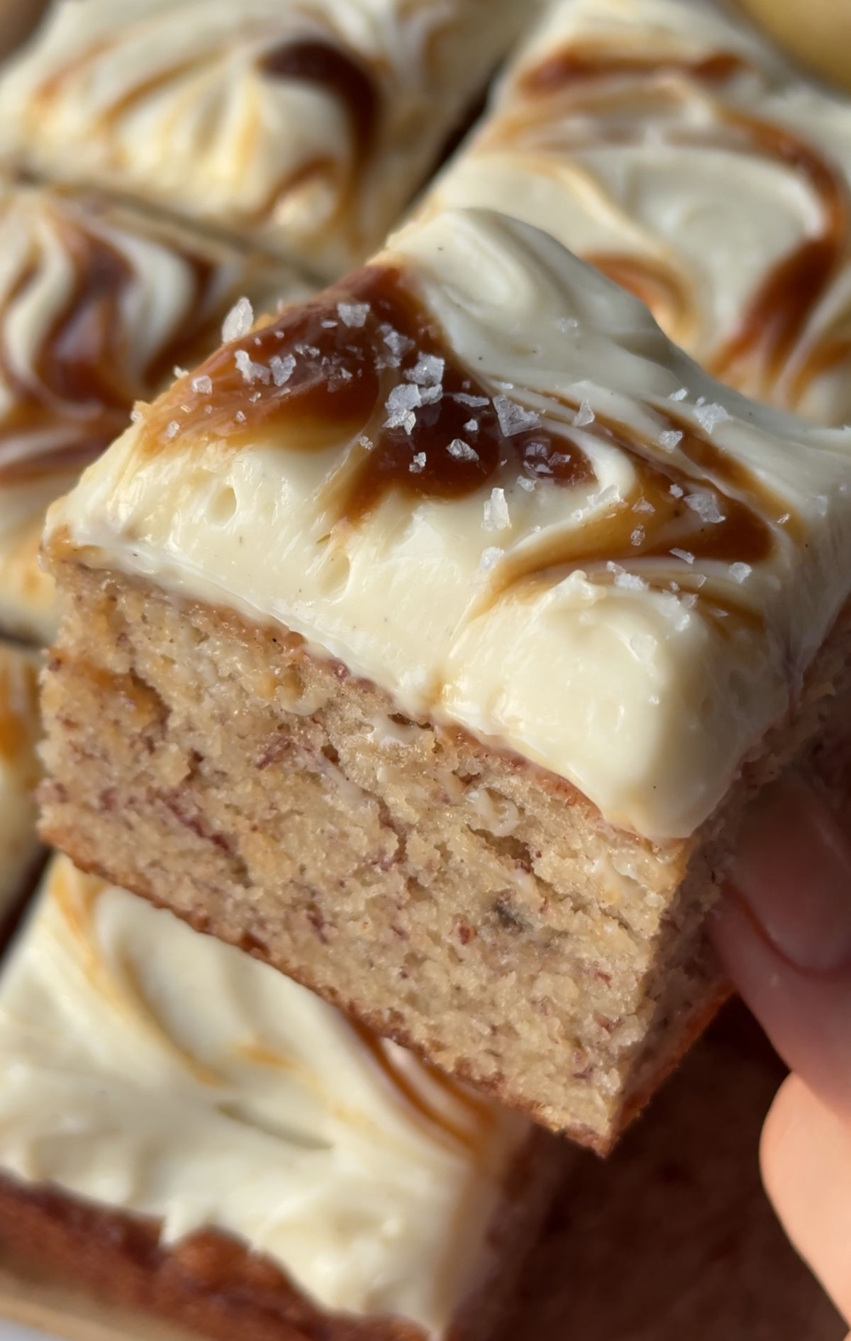 A hand holding a piece of frosted vegan banana cake.