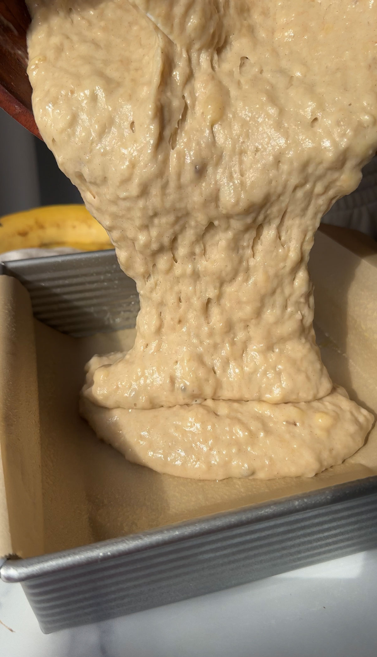 Vegan banana cake batter being poured into a lined pan