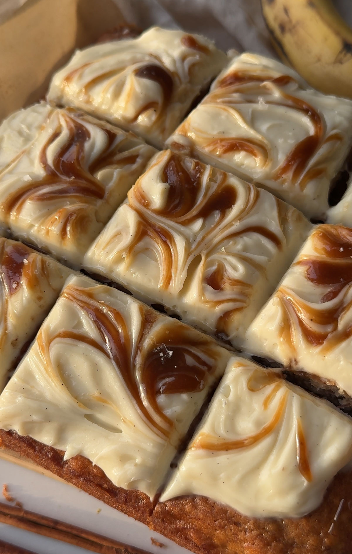 Sliced banana cake with cream cheese frosting with caramel swirl on top.