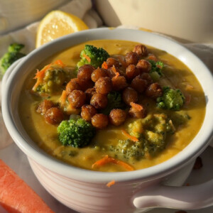 A bowl of vegan broccoli cheddar soup topped with crispy chickpeas on a kitchen countertop.