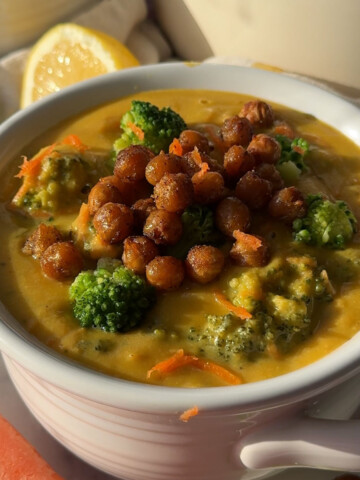 A bowl of vegan broccoli cheddar soup topped with crispy chickpeas on a kitchen countertop.
