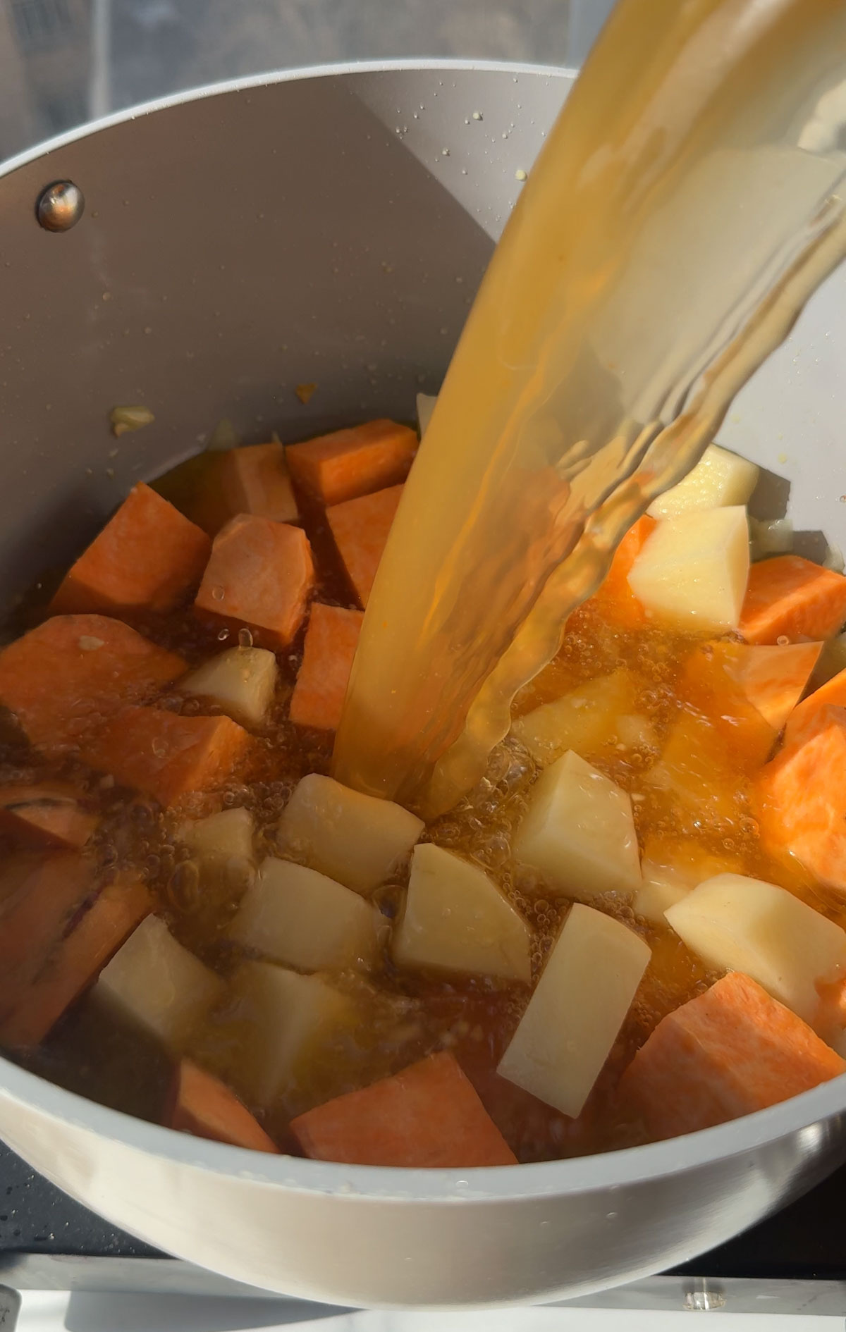 Vegetable broth being poured over russet and sweet potato chunks.
