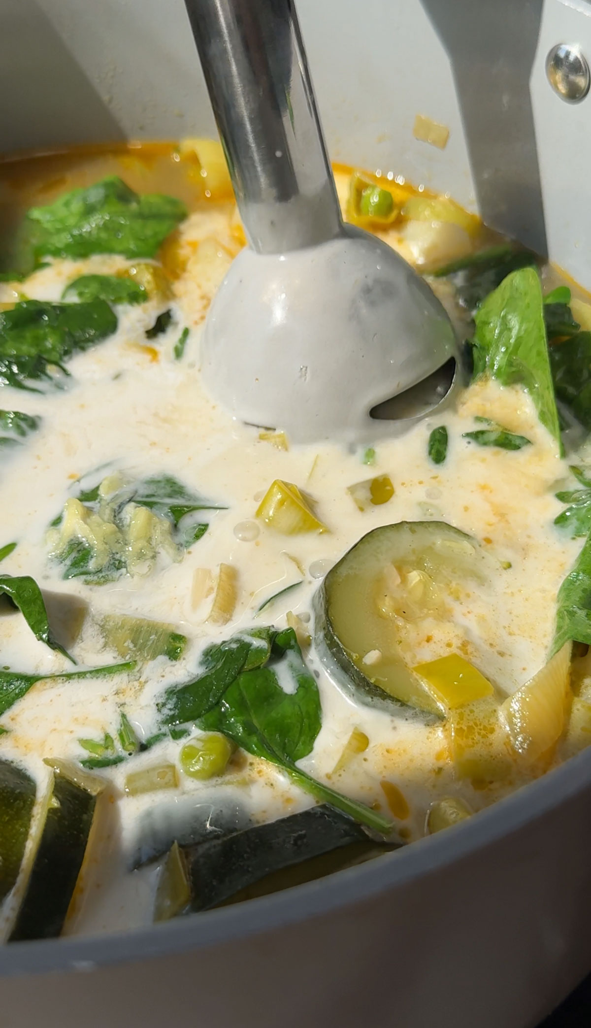 Green soup being blended with an immersion blender.