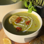 Green soup in a white bowl drizzled with some white sauce and chili oil.